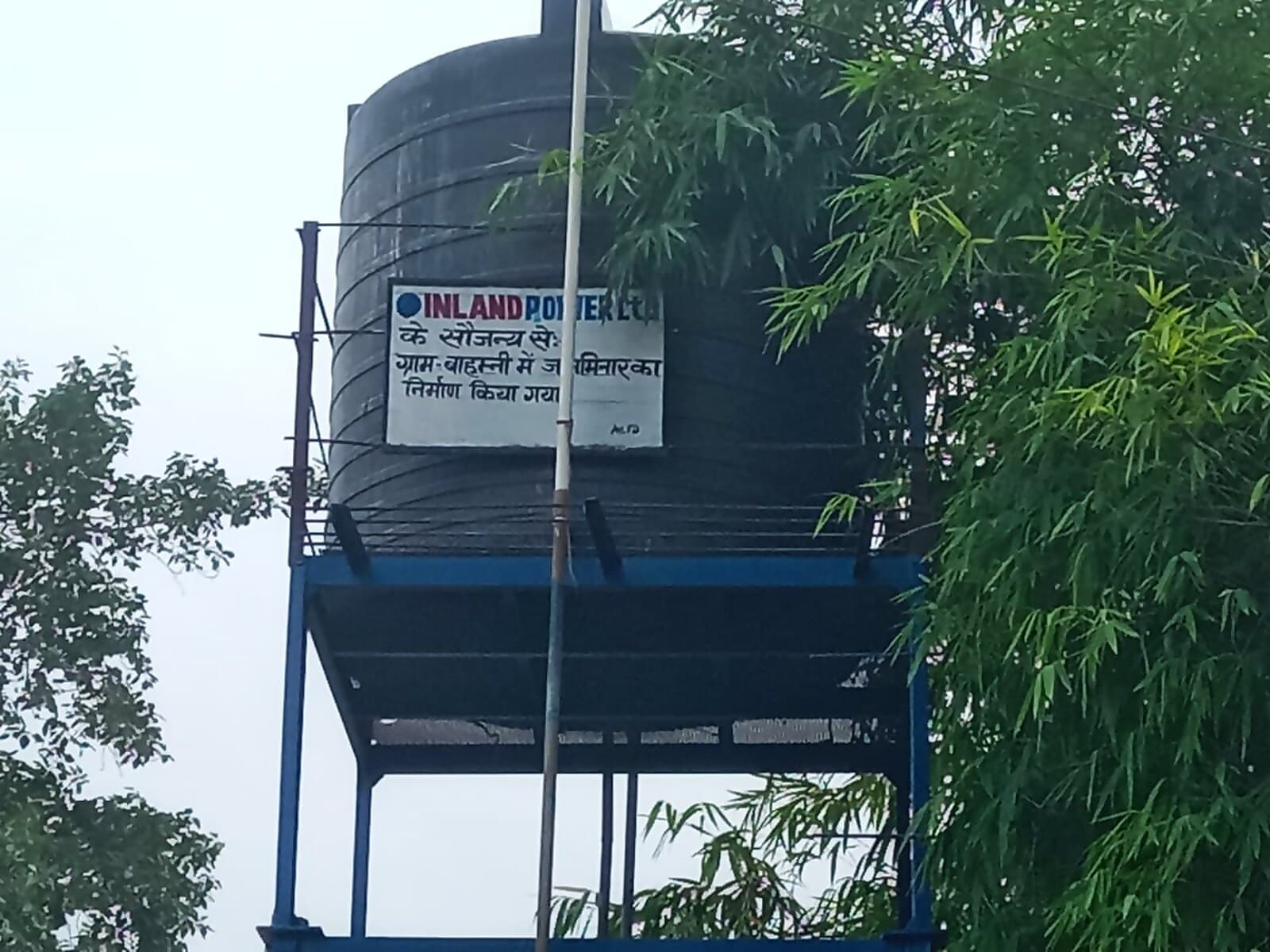 A new Inland Power-branded overhead water tank on a concrete plinth, supplying a village near Inland Nagar.