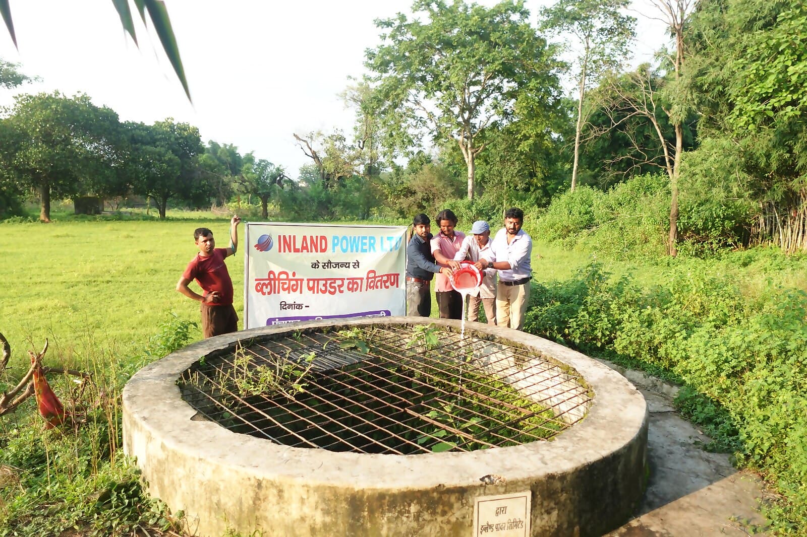 A village open well fitted with a protective cover under Inland Power's CSR programme, beside a bleaching-powder distribution banner.